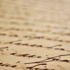 Extreme closeup of old handwritten manuscript on yellowed paper with cursive ink writing, shallow depth of field soft blurred background, vintage document texture history, literature, poetry, archival